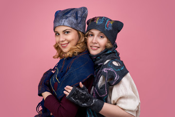 Studio portrait of two friends. Women in winter clothes in a hat, mittens smiling widely at the camera.