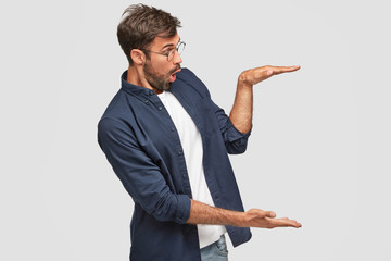 Shocked terrible guy gestures wth both hands, shows height or size of thing against white...