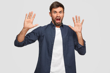 Annoyed unshaven man feels aversion, has disgusted expression, asks not bother him, keeps palms in front, looks with irritation, isolated over white background. Negative human emotions and feelings - obrazy, fototapety, plakaty