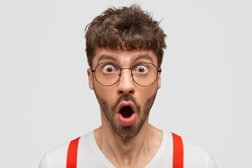Close up portrait of handsome stupefied unshaven young guy keeps jaw dropped, says wow as found...