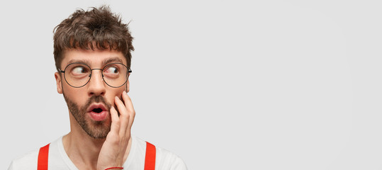 Surprised astonished young Caucasian man looks mysteriously and surprisingly aside, opens mouth,...