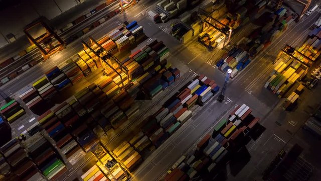 Aerial hyperlapse - Night shot of busy port. Shipping containers being transported with lifting cranes and network trucks to their final destination