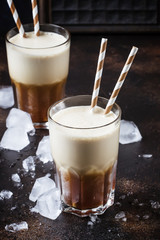 Cold frappe coffee with ice and foam in large glasses on brown background, selective focus