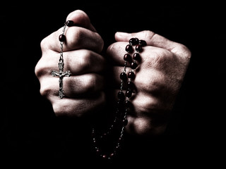 Female hands praying holding a rosary with Jesus Christ in the cross or Crucifix on black...