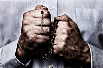 African American male hands praying holding a beads rosary with Jesus Christ in the cross or Crucifix on black background. Mature Afro American man with Christian Catholic religious faith - obrazy, fototapety, plakaty