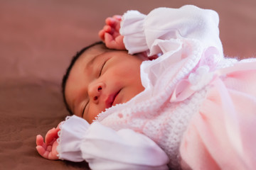 Cute two weeks old newborn baby girl wearing soft pink knit clothes, sleeping peacefully in bed