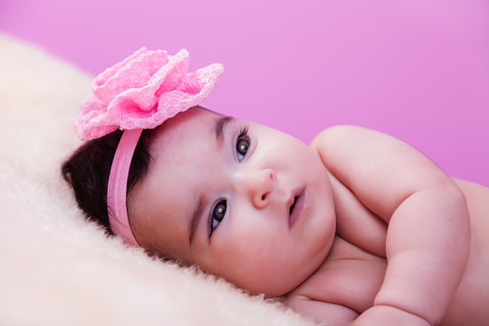 Cute, pretty, happy, chubby baby girl portrait, without clothes, naked or nude, on a fluffy blanket. Pink flower headband. Looking up. Four months