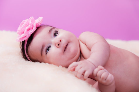 Cute, pretty, happy, chubby baby girl portrait with a big naughty smile. Naked or nude on fluffy blanket. Pink flower headband. Four months