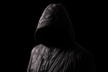 Naklejka na ściany i meble Scary and creepy man hiding in the shadows, with the face and identity hidden with the hood, and standing in the darkness. Low key, black background. Concept for fear, mystery, danger, crime, stalker