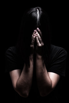 Emotional woman crying and covering the face with the hands hiding the tears, on a black or dark background. Concept for victim, depression, pain, grief, mourn, despair, sadness, fear.