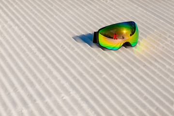 Ski goggles laying on a new groomed snow and empty ski slope