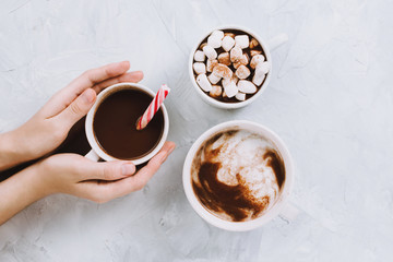 Three cups of vegan hot chocolate or cocoa with different toppings on grey