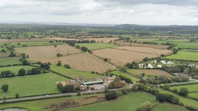 Aerial view, fast panning move. Plains, houses, pond in Cheshire. Cars on road in background