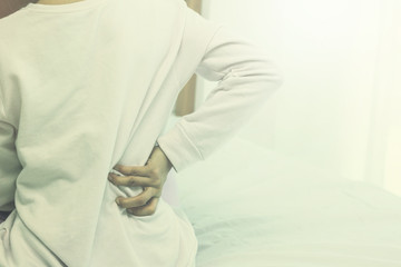 Asian woman back pain and sit on bed in bedroom in the morning.color tone