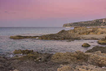 Sunset on the rocky coast with anchored sailboat