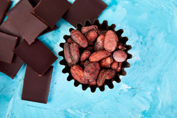 Cocoa beans background on blue table. Dark chocolate pieces