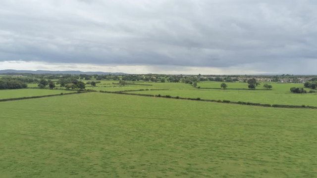 Aerial view, rise up and pan move. Tarvin small town among plains in Cheshire. Rainy clouds over hills in background