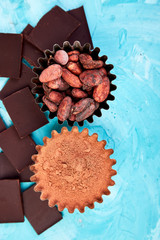 Cocoa beans background on blue table. Dark chocolate pieces