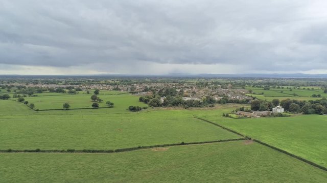 Aerial view, tilt down and zoom out move. Tarvin small town among plains in Cheshire. Rain over hills in background