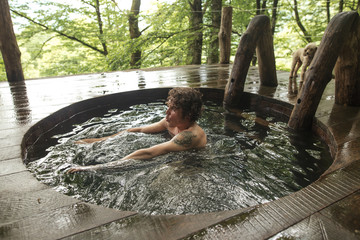 young good looking male is taking a dip in the hot tub. close up side view photo. amazing forest on...