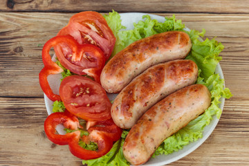 Grilled sausages with fresh vegetables on wooden table