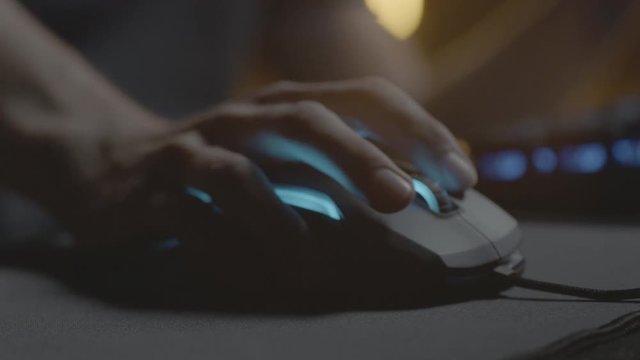 Video gamer or hacker. Hand on computer mouse with RGB backlight. Close-up dolly panning. Shallow depth of field