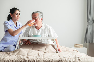 Young attractive nurse feeding breakfast to senior man in bed