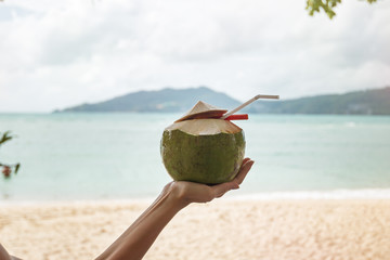 coconut milk/ coconut with coconut milk and a straw in a woman's hand on the background of the beach and the sea in Thailand