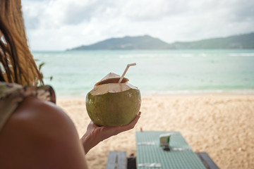 coconut with milk/ coconut with coconut milk and a straw in a woman's hand on the background of the...