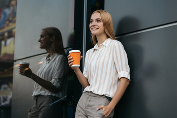 Portrait of successful business woman wearing formal clothing drinking coffee, thinking about project near business centre. Coffee break concept. Attractive female with beautiful smile waiting taxi.  - obrazy, fototapety, plakaty