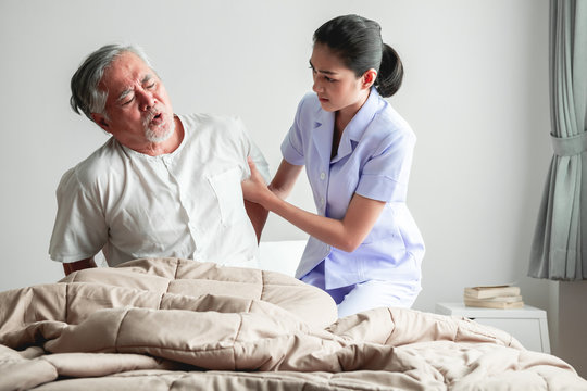 Senior man in bed trying to get up and nurse helping him.