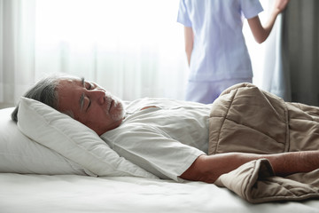 Senior man sleeping in bed and nurse open curtain.