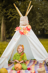 Little girl lying and playing in a tent, children's house wigwam in park Autumn portrait of cute curly girl. Harvest or Thanksgiving. autumn decor, party, picnic. Child in halloween costume. © MartaKlos