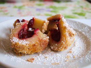 Plum dumpling sprinkled with powdered sugar on a white plate.