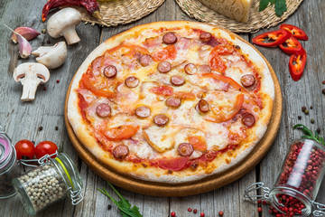 Pizza with tomatoes, mozzarella cheese, black olives and basil. Delicious italian pizza on wooden pizza board.