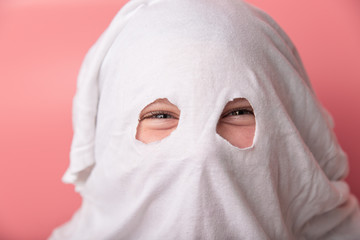 young child dressed in a ghost costume for halloween on pink background