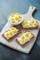 Homemade Crispbread toast with Cottage Cheese and Pineapple on white wooden board.