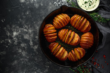Hasselback baked potatoes served in cast-iron pan with sour cream salt, pepper and herbs