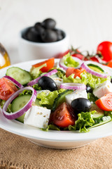 Fresh Greek salad made of cherry tomato, ruccola, arugula, feta, olives, cucumbers, onion and spices. Caesar salad in a white bowl on wooden background. Healthy organic diet food concept.