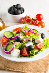 Fresh Greek salad made of cherry tomato, ruccola, arugula, feta, olives, cucumbers, onion and spices. Caesar salad in a white bowl on wooden background. Healthy organic diet food concept.