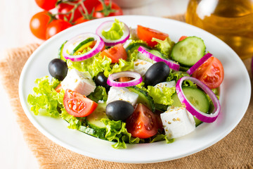 Fresh Greek salad made of cherry tomato, ruccola, arugula, feta, olives, cucumbers, onion and spices. Caesar salad in a white bowl on wooden background. Healthy organic diet food concept.