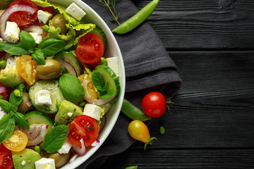 Healthy low calories salad with lettuce, heirloom tomatoes, avocado, feta cheese, red onion, cucumber, sweet peas, olives, thyme, mint and basil.