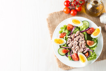 Fresh fish tuna salad made of tomato, ruccola, tuna, eggs, arugula, crackers and spices. Caesar salad in a white bowl on wooden background
