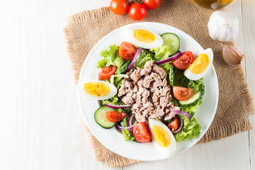 Fresh fish tuna salad made of tomato, ruccola, tuna, eggs, arugula, crackers and spices. Caesar salad in a white bowl on wooden background