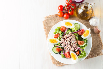 Fresh fish tuna salad made of tomato, ruccola, tuna, eggs, arugula, crackers and spices. Caesar salad in a white bowl on wooden background