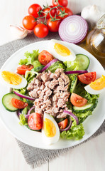 Fresh fish tuna salad made of tomato, ruccola, tuna, eggs, arugula, crackers and spices. Caesar salad in a white bowl on wooden background