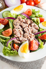 Fresh fish tuna salad made of tomato, ruccola, tuna, eggs, arugula, crackers and spices. Caesar salad in a white bowl on wooden background