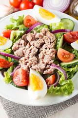Fresh fish tuna salad made of tomato, ruccola, tuna, eggs, arugula, crackers and spices. Caesar salad in a white bowl on wooden background