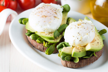 Avocado toast, cherry tomato on wooden background. Breakfast with toast avocado, vegetarian food, healthy diet concept. Healthy sandwich with avocado and poached eggs.