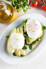Avocado toast, cherry tomato on wooden background. Breakfast with toast avocado, vegetarian food, healthy diet concept. Healthy sandwich with avocado and poached eggs.
